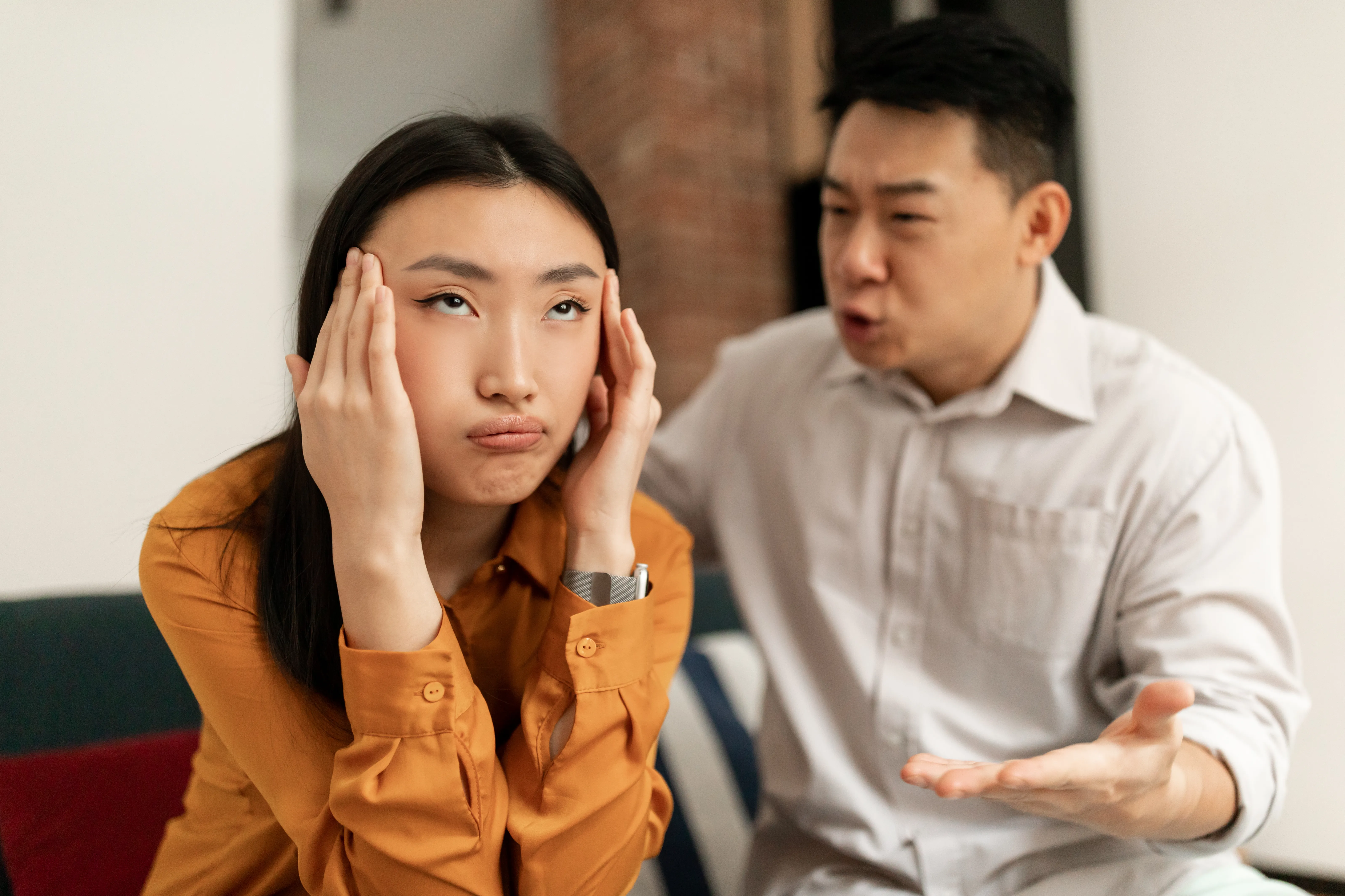 A woman rubbing her temples as a man argues with her