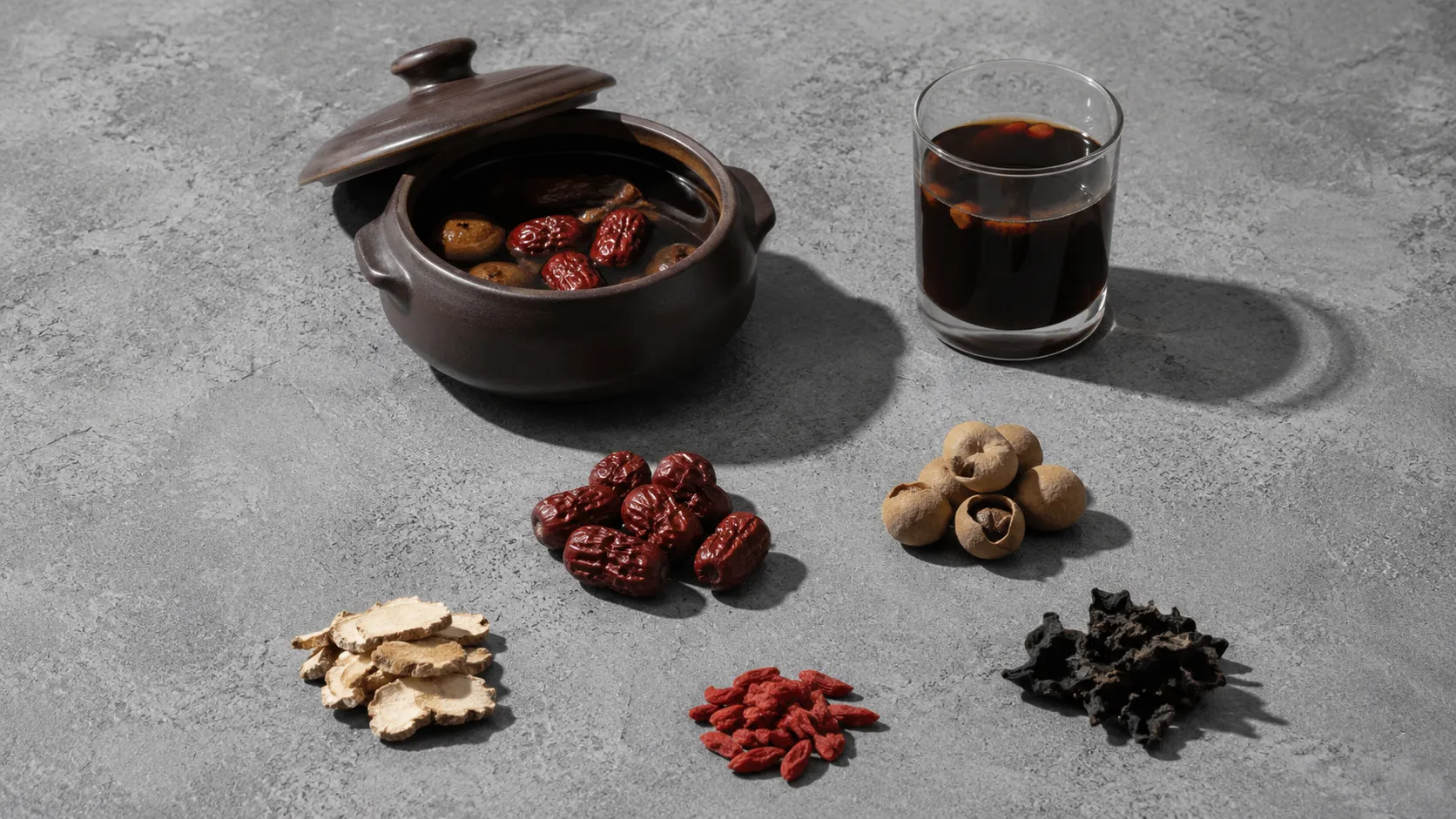 A month of Malaysian confinement food ingredients laid out on a bare surface: red dates, dried longan, sliced ginger, wolfberries and a clay soup pot