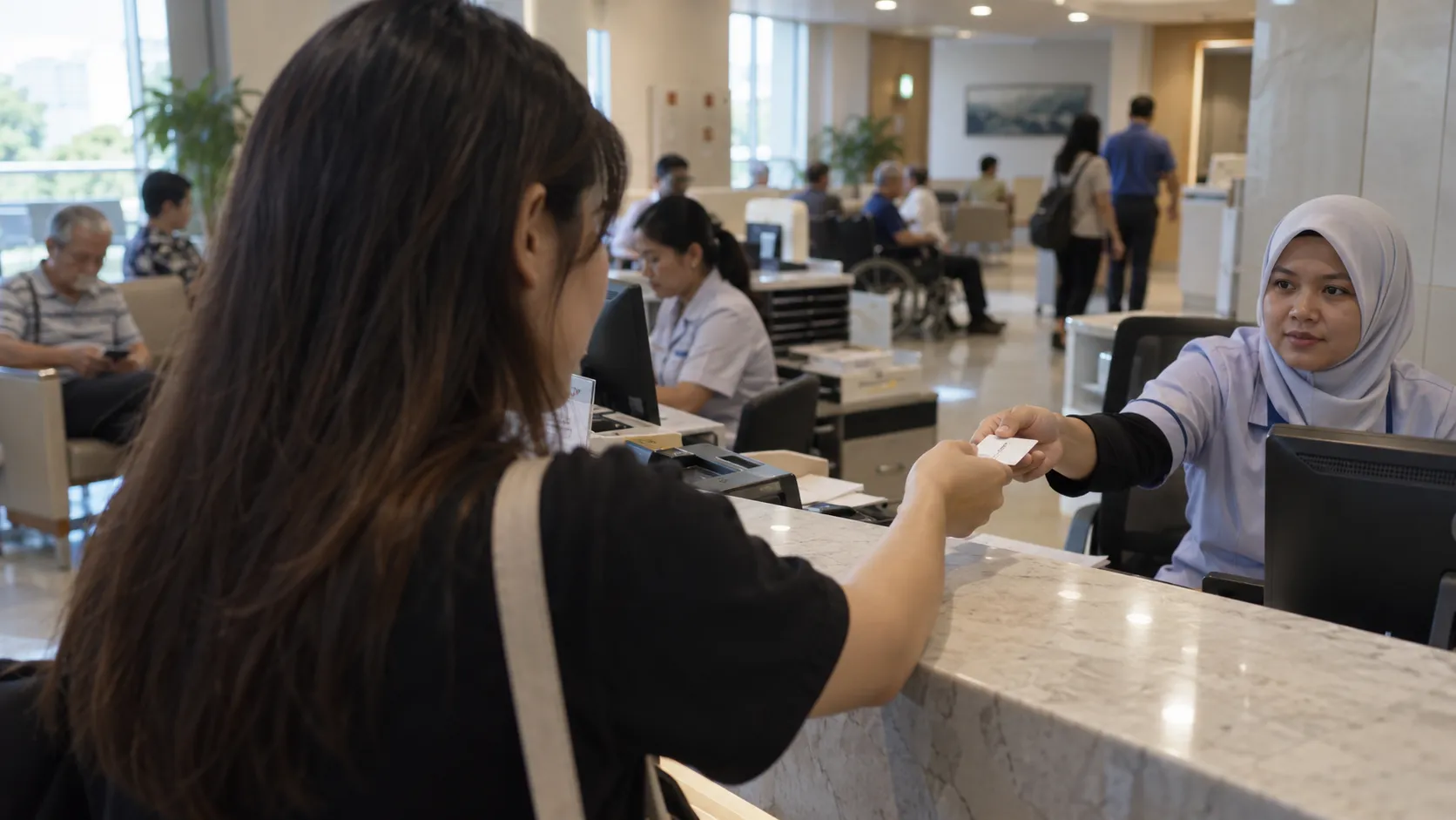 A young Malaysian woman handing her medical card across the admissions counter at a private hospital