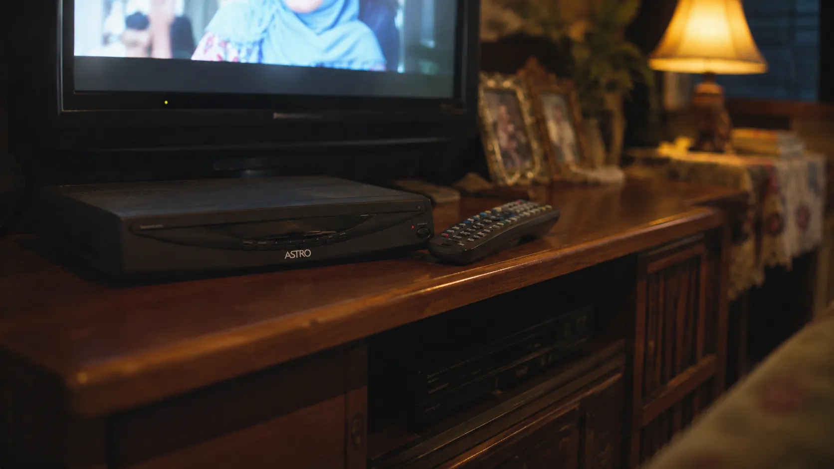 An Astro decoder box and remote on a TV console in a warmly lit Malaysian living room