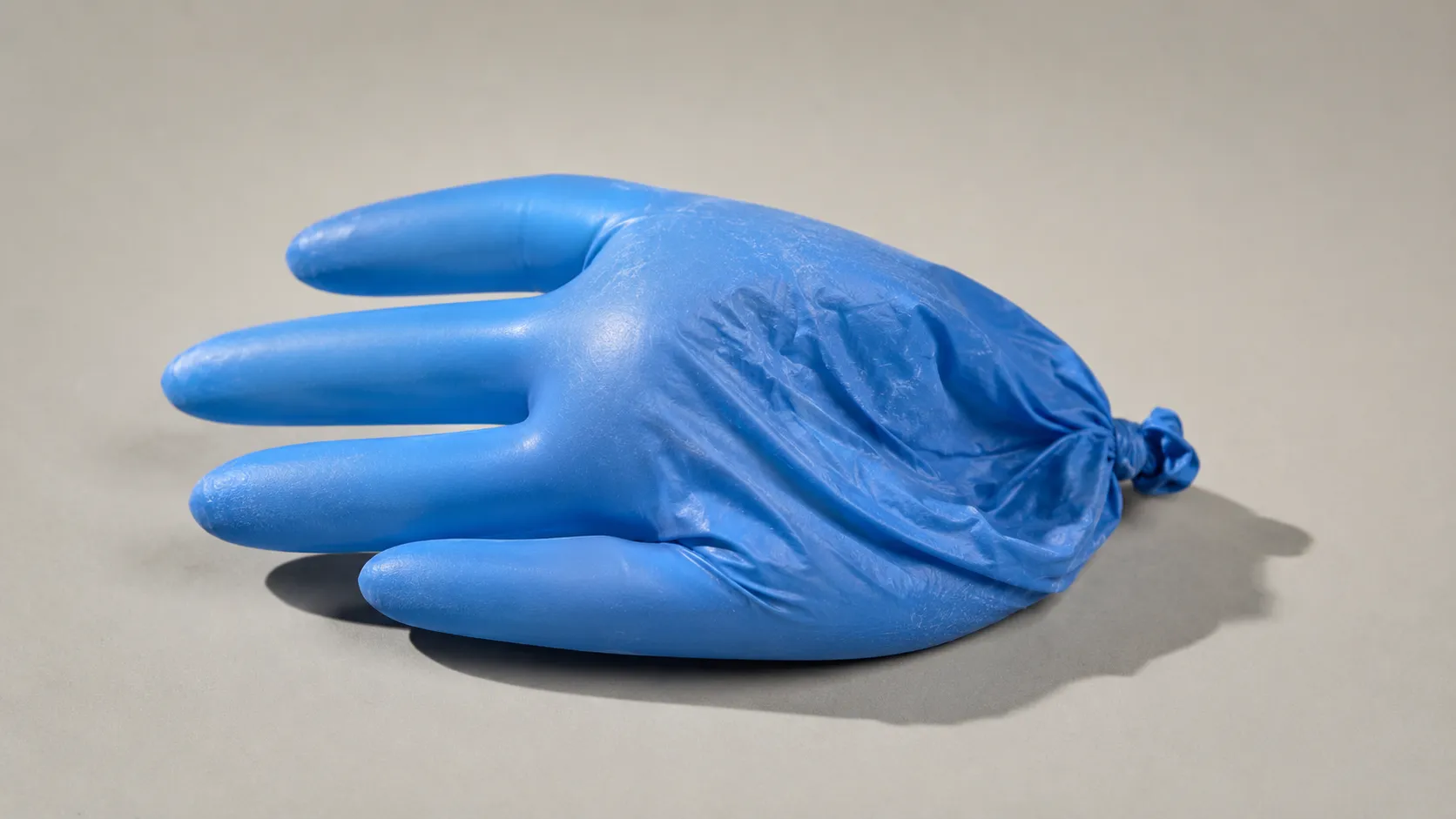 A blue nitrile glove inflated like a balloon and half deflated, lying on a studio backdrop under hard light